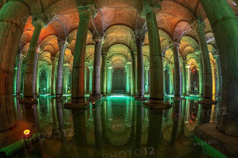 Ancient underground water reservoir with many columns reflecting on the water surface and illuminated by colorful lights, creating a magical atmosphere