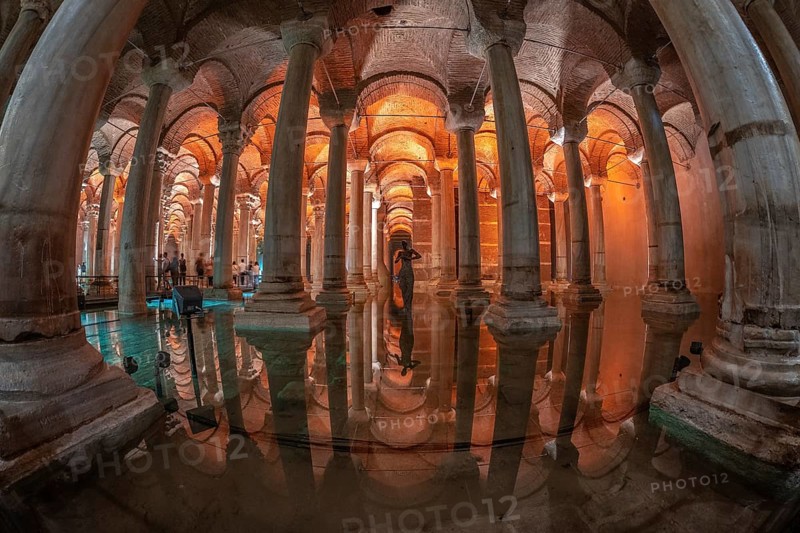 Ancient underground basilica cistern reflecting on water surface with tourists and medusa head sculpture in istanbul, turkey