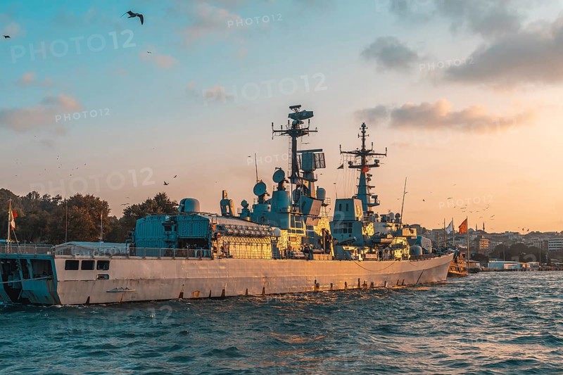 Modern warship gliding through the tranquil sea near istanbul, turkey, under a stunning golden hour sky filled with warm hues