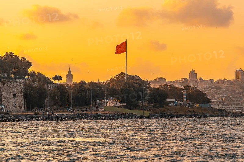 Scenic sunset view of istanbul's cityscape, featuring the prominent galata tower and a waving turkish flag, creating a patriotic and picturesque scene