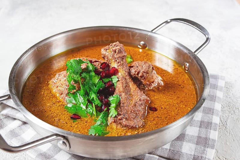 Fesenjan, an Iranian dish, stewed chicken, in a nut-pomegranate sauce, in a saucepan, light background, homemade, no people