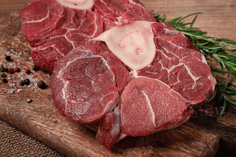 Knuckle on the bone, raw meat for ossobuco, on a wooden chopping board, with a sprig of rosemary, and spices, top view, no people