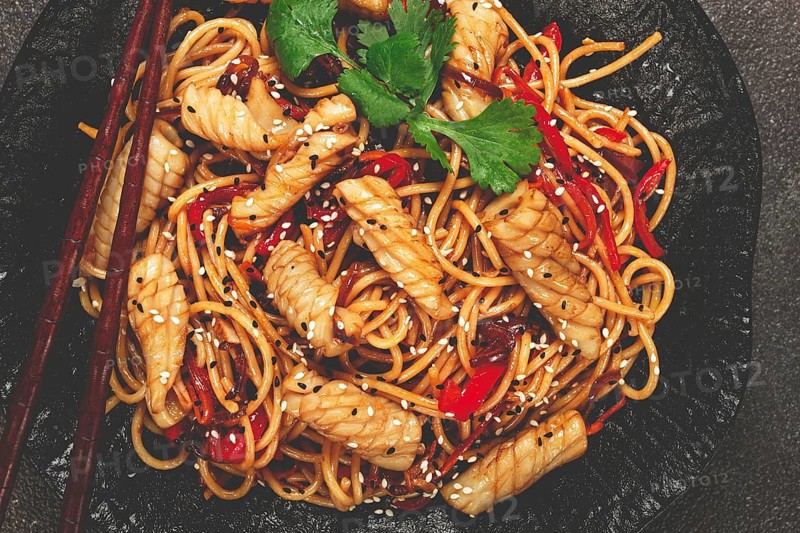 Udon noodles, with squid and vegetables, on a black plate, homemade, no people