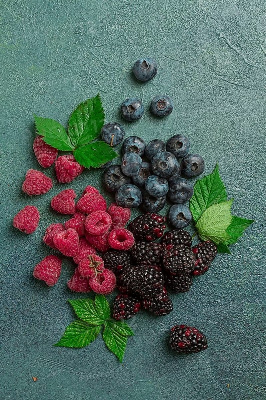 A mix of ripe berries, with leaves scattered on the table, raspberries, blackberries, blueberries, food background