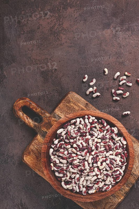 Variegated beans, red with white spots, raw in a wooden bowl, top view, no people