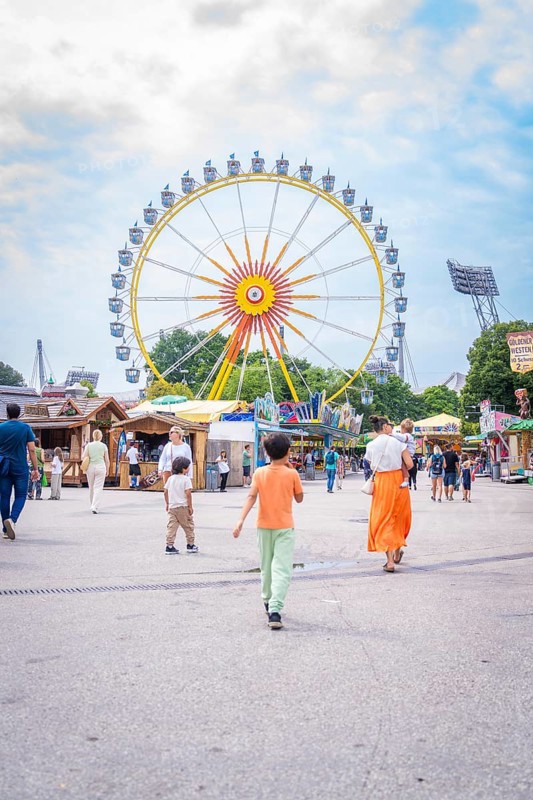 People on a square in an amusement park with a large Ferris wheel in the background, Olympiapark, Munich, Germany