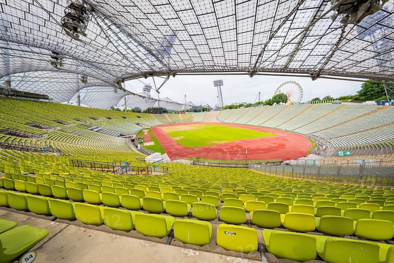 Overview of the stadium with green seats and red running track, framed by an impressive roof design, Olympiapark, Munich, Germany