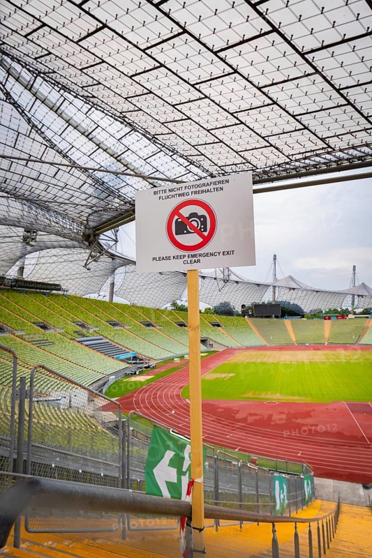 View of stadium grandstand and running track, dominated by a metal grid construction and prohibition sign in the foreground, Olympiapark, Munich, Germany