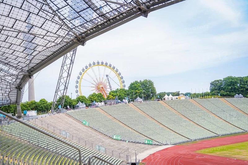 Open stadium with a view of a Ferris wheel in the background and green rows of seats, Olympic Park, Munich, Germany