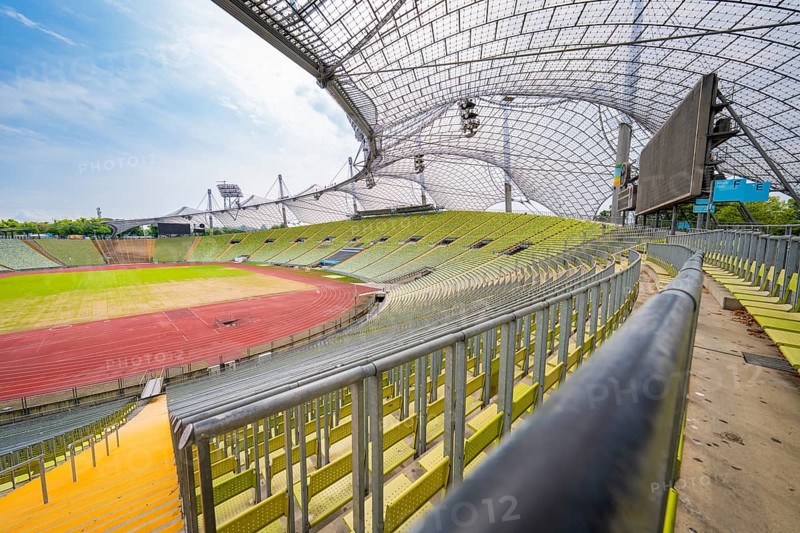 Empty modern stadium with green seats and striking glass roof under a blue sky, Olympiapark, Munich, Germany