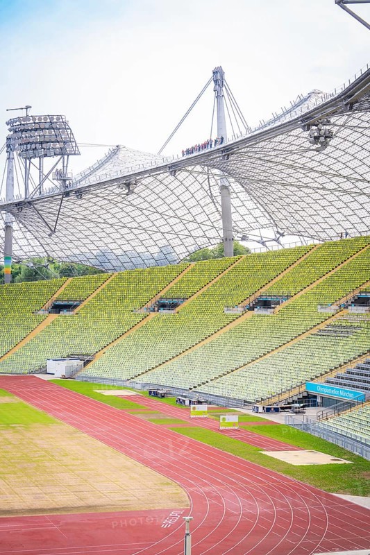 Partial view of a modern stadium with green rows of seats and red running track, Olympic Park, Munich, Germany