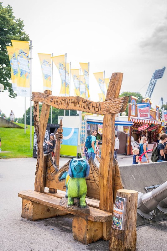 Wooden bench with colourful bear figure and lettering in amusement park with background of visitors, Olympic Park, Munich, Germany