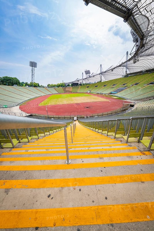 View down the yellow steps to an empty stadium with wide stands and running track, Olympiapark, Munich, Germany