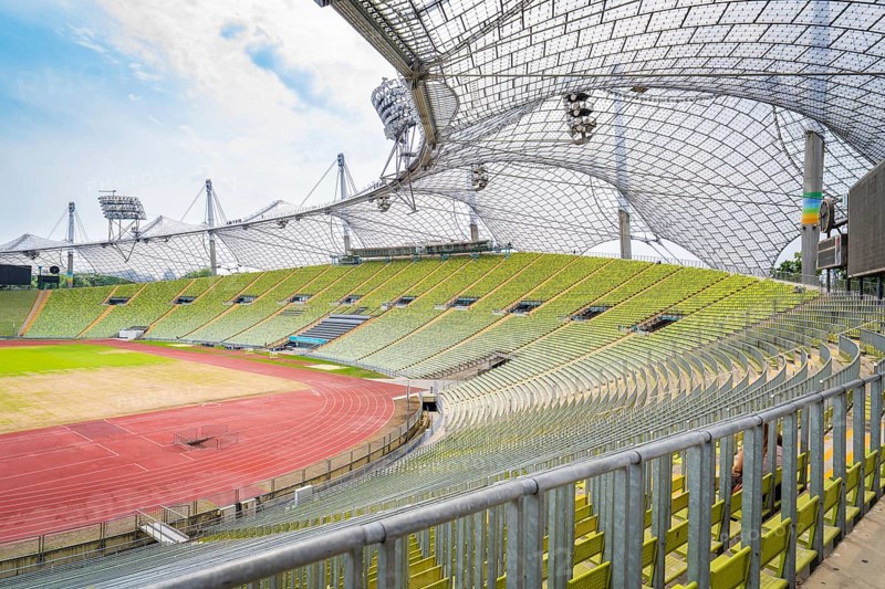 Large stadium with empty green stands and striking roof structure in the sunlight, Olympiapark, Munich, Germany