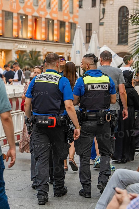 Two security guards in uniforms walking through a busy street, Munich, Germany