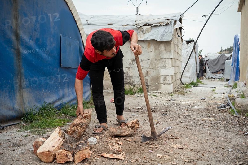 A young displaced Syrian man cutting firewood to use for heating inside a refugee camp. Aleppo, Syria February 9, 2018, Aleppo, Syria