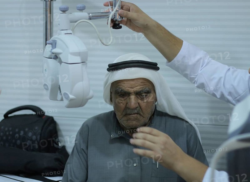 An ophthalmologist performing an eye examination for an elderly displaced man using an ophthalmoscope inside a mobile medical clinic. Aleppo, Syria May 10, 2017, Aleppo, Syria
