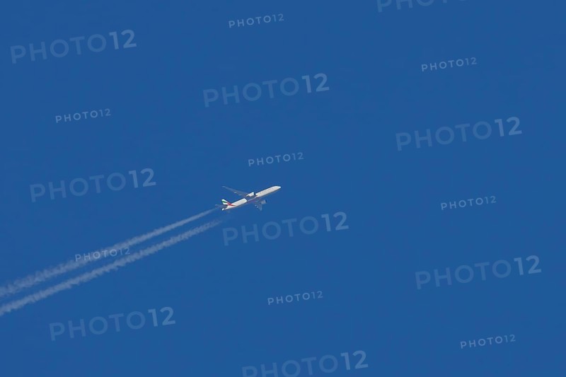 Airbus jet passenger aircraft of Emirates airlines flying with vapour trails or contrails behind in a blue sky, England, United Kingdom