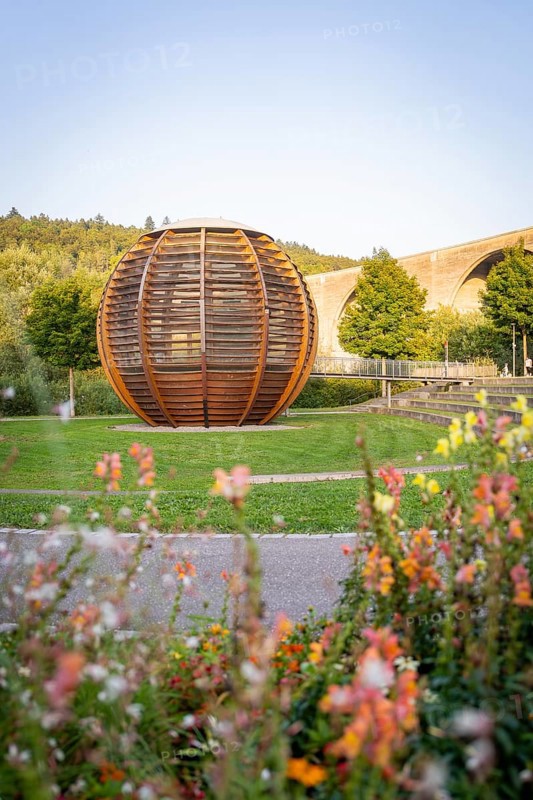 Wooden sculpture in a park with flowers and bridge in the background under a clear sky, Nagold, district of Calw, Black Forest, Germany