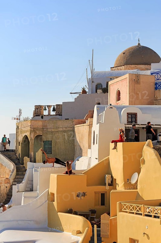 Tourists pose on colourfully painted houses on the hillside, picturesque village of Oia, Thira, Santorini, Cyclades, Greece