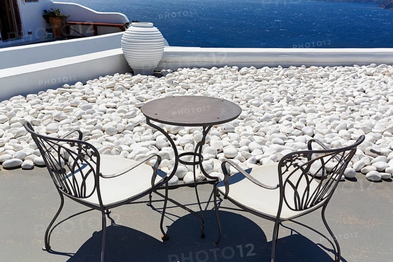 White gravelled area, wrought-iron table and two chairs, vase on a terrace by the sea, Oia, Santorini, Cyclades, Aegean Sea, Greece