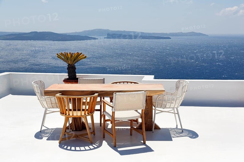 Wooden table and various chairs on a white terrace by the sea, view of the caldera, Oia, Santorini, Cyclades, Aegean Sea, Greece