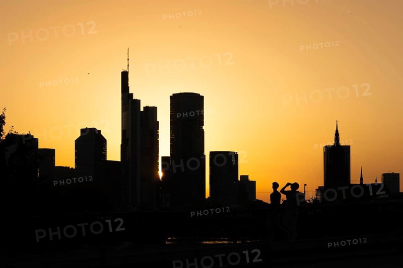 Two men cross the rafter bridge over the Main in the evening as the sun sets behind the Frankfurt banking skyline, Frankfurt am Main, Hesse, Germany