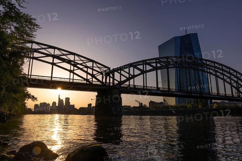 The sun stands over the Frankfurt banking skyline and illuminates the glass façade of the European Central Bank (ECB), Frankfurt am Main, Hesse, Germany