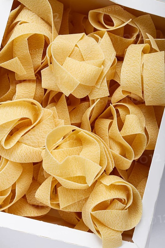Raw pappardelle pasta, pasta nests, in a paper box, top view, no people