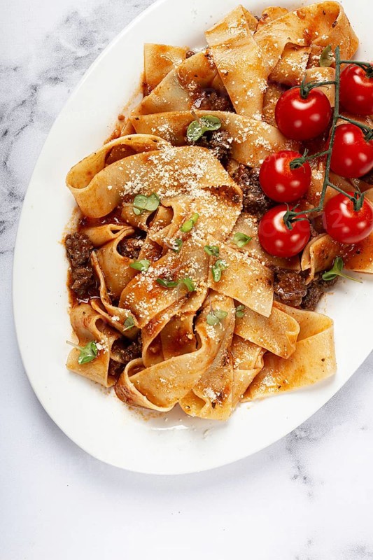 Pappardelle pasta with bolognese sauce, topped with parmesan cheese and cherry branch, homemade, no people
