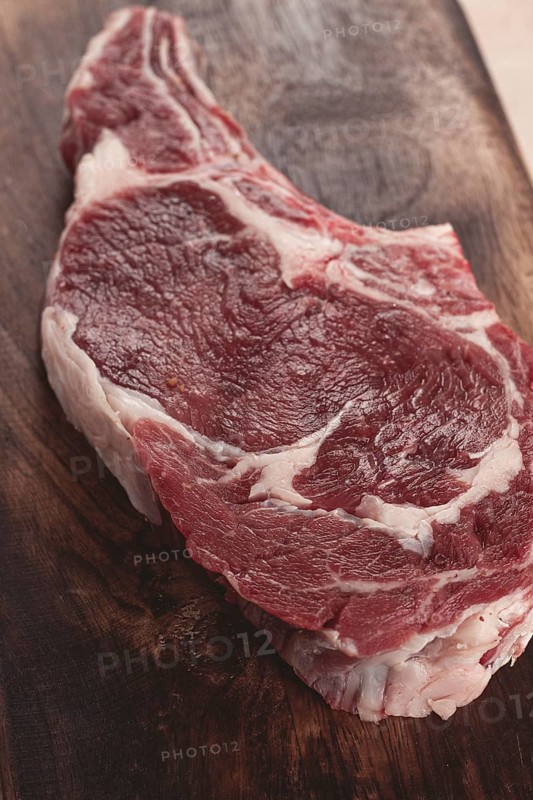 Raw rib eye steak, cowboy steak, wooden chopping board, marble table, top view, no people