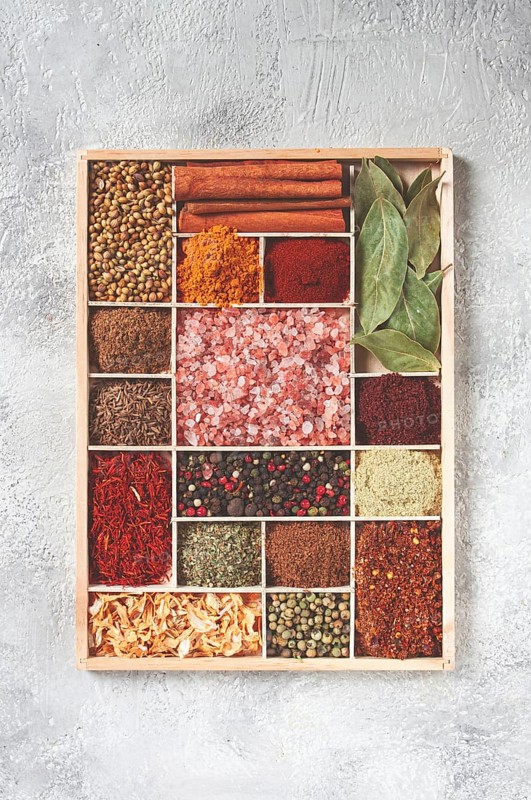 An assortment of spices laid out on a wooden tray, arranged in wooden compartments, top view
