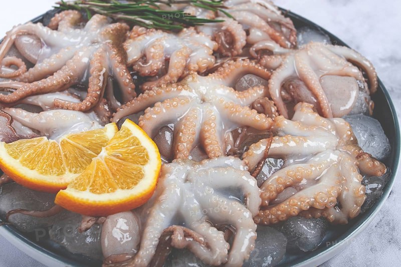 Fresh baby octopuses on ice, garnished with lemon and rosemary, on a marble table, no people