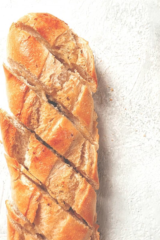 Garlic bread, baguette with garlic butter and herbs, on a light table, top view