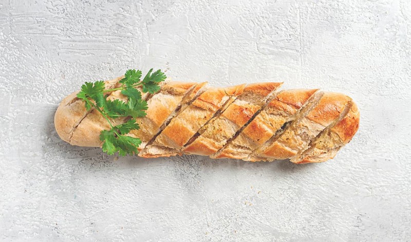 Garlic bread, baguette with garlic butter and herbs, on a light table, top view