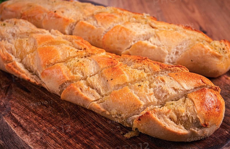Garlic bread, baguette with garlic butter and herbs, on a wooden board, with herbs and garlic cloves
