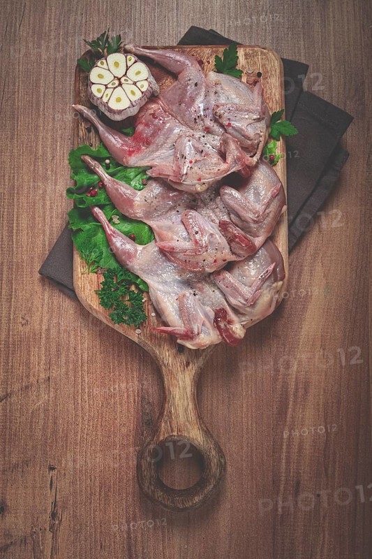 Raw quail meat, on a cutting board, with spices and herbs, top view