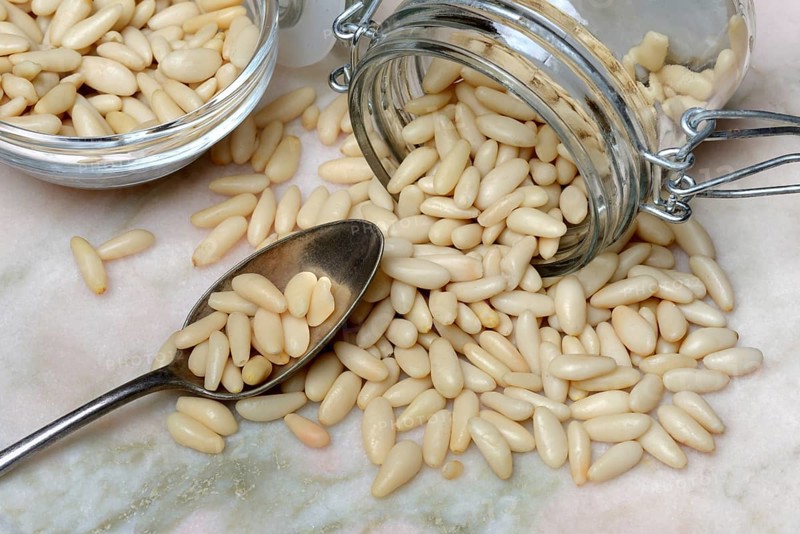 Pine nuts in glass container and spoon, Pinus pinea