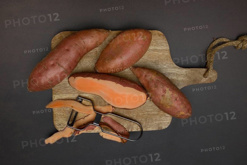 Sweet potatoes with potato peeler on wooden board, Ipomoea batatas