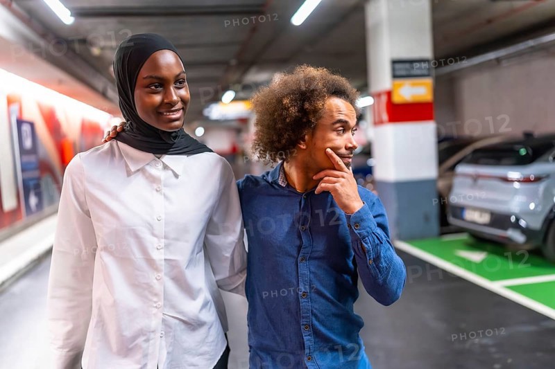 Diverse young couple happily walking arm in arm through a modern underground parking garage, sharing a moment of connection and togetherness in an urban environment
