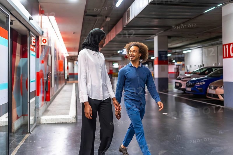 Diverse young couple walking hand in hand through an underground parking garage, sharing a loving moment and smiling, representing connection and modern urban life