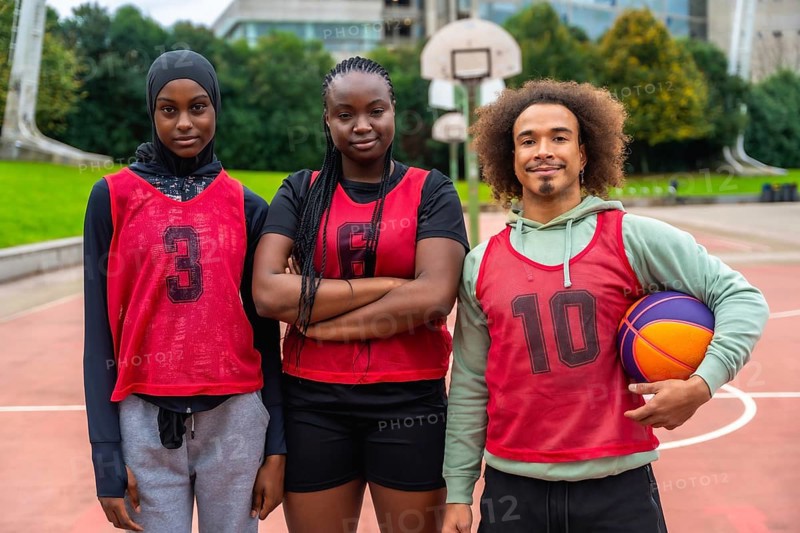 Diverse group of young adult basketball players standing on an outdoor court, proudly wearing sports bibs and a hijabi woman embracing inclusivity in sports