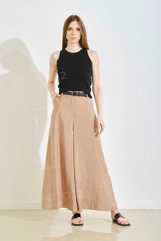 A young woman showcases a stylish outfit with a fitted black tank top and elegant beige wide-leg pants. She stands confidently in a bright, minimalist studio, perfect for practical fashion