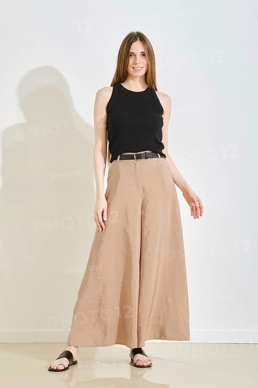A young woman stands confidently in a trendy outfit, showcasing wide-legged beige pants and a black sleeveless top. This stylish look emphasizes comfort and practicality, perfect for casual settings