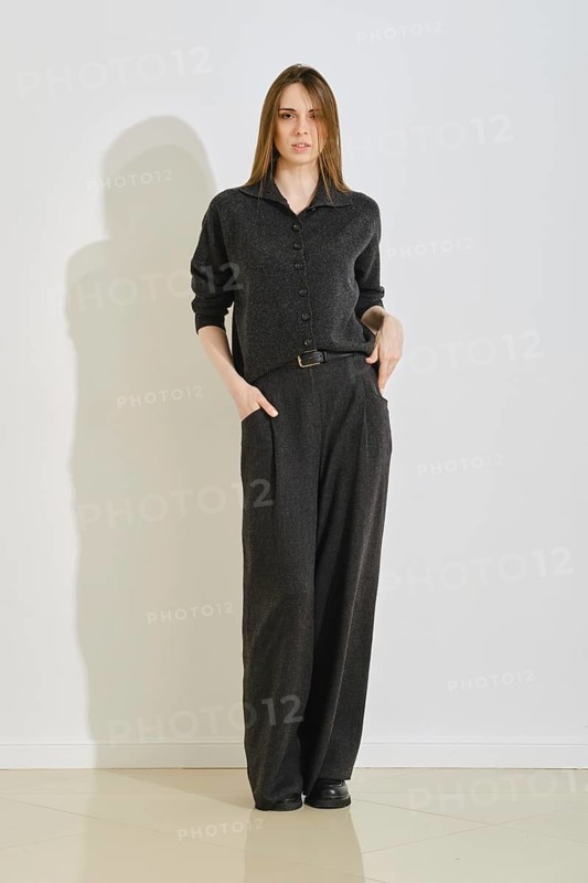 A woman stands in a trendy dark outfit, featuring a button-up top and loose pants. She showcases convenience and style, perfect for a day in the city or casual gatherings