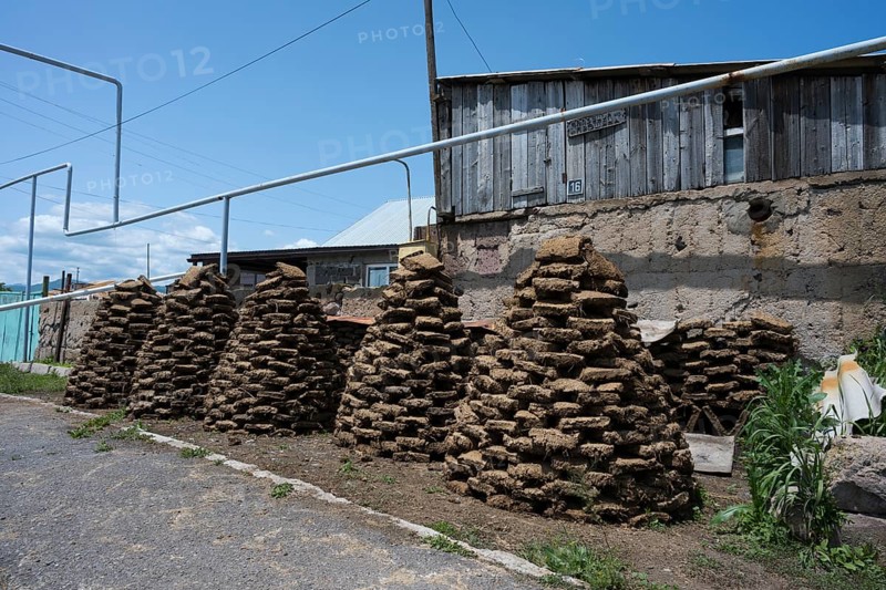 Stacked dried cow bricks in front of a wooden house under blue sky, near Sewan, Gegharkunik province, Armenia