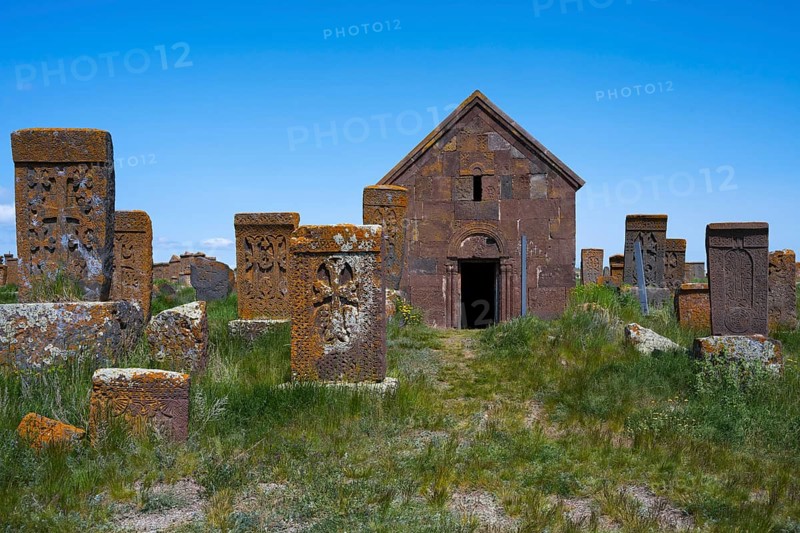Church surrounded by ancient tombstones in a green setting under a blue sky, crossstones, khachkars, world's largest khachkar field, Noratus cemetery, Noradus, Gegharkunik province, Armenia