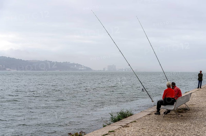 Anglers on Ponte 25 de Abril, 3.2 km long bridge in Portugal with a 2278 meter long suspension bridge across the Tagus, cloudy and rainy weather, third-longest suspension bridge with combined road and rail traffic, Lisbon, Portugal