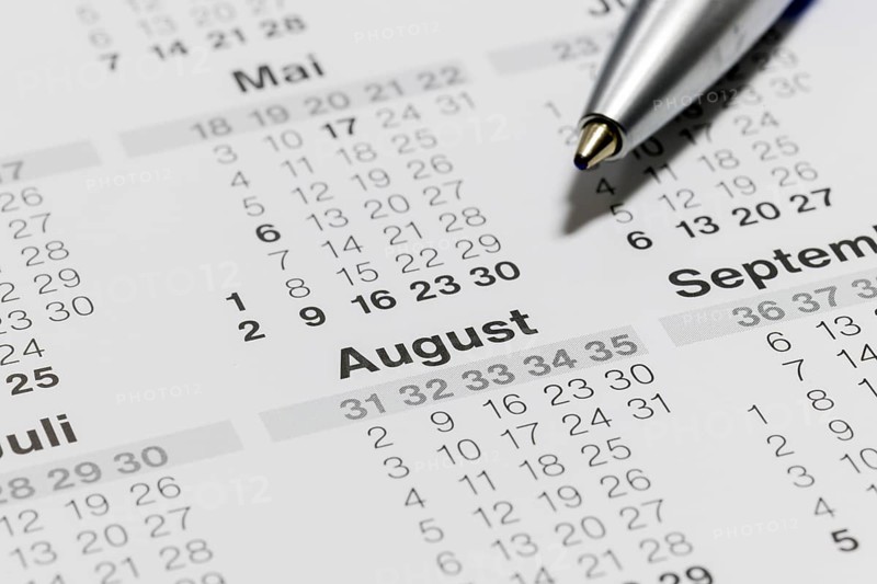 Close-up of a calendar with ballpoint pen pointing to the month of August