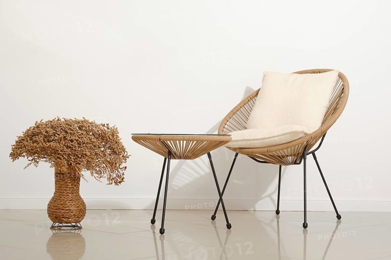 A cozy chair with soft cushioning sits next to a small, stylish table in a contemporary living area. A decorative vase filled with dried flowers adds a touch of nature to the warm design